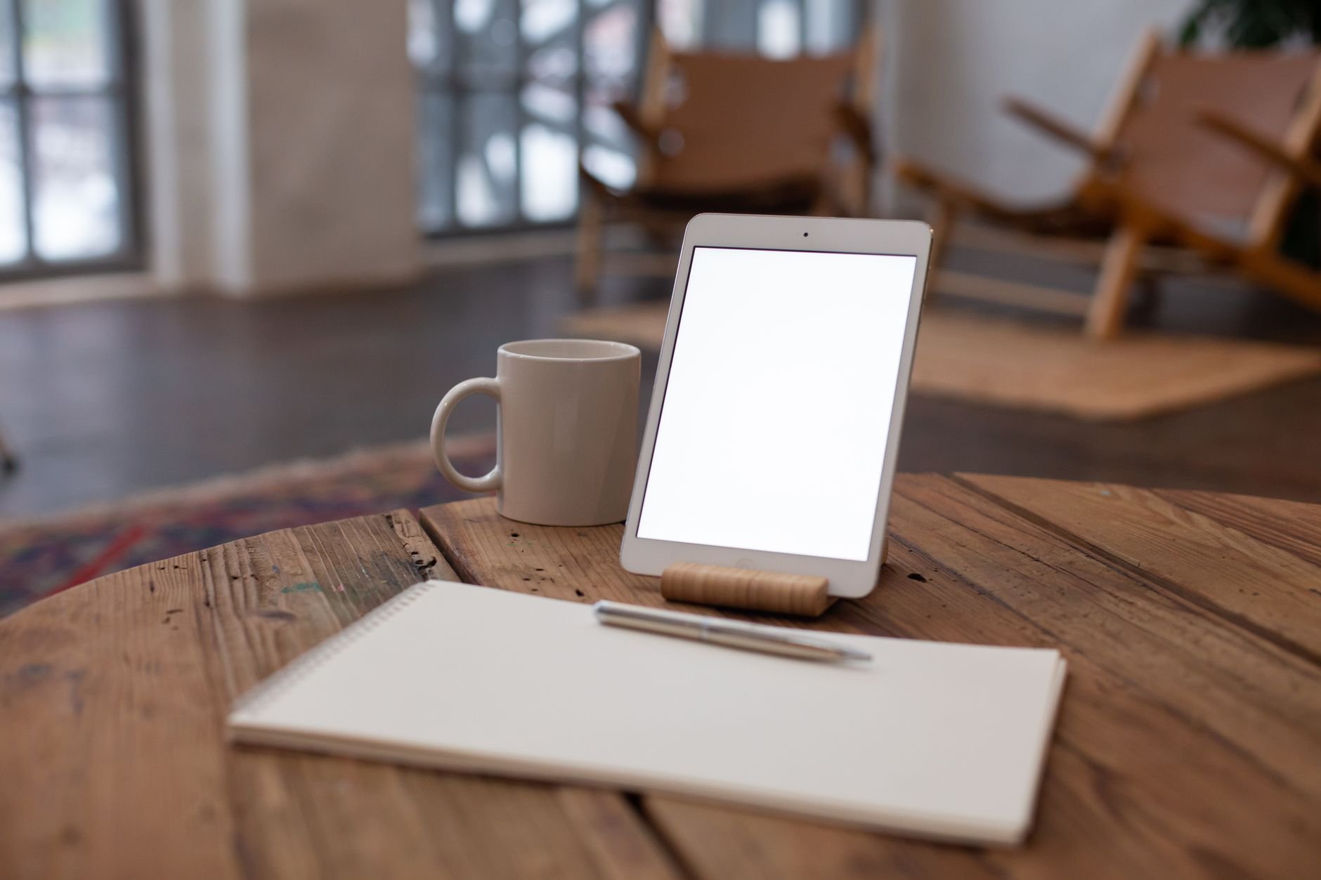 A digital tablet and coffee mug on a rustic table in a cozy indoor setting.